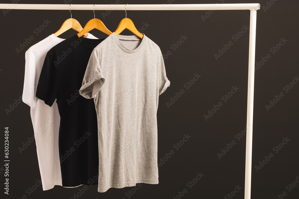 Naklejka premium Three t shirts on hangers hanging from clothes rail and copy space on black background