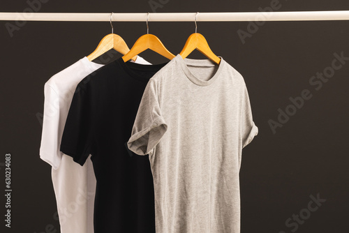 Three t shirts on hangers hanging from clothes rail and copy space on black background