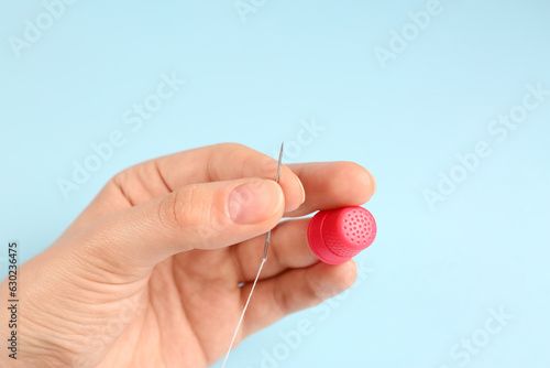 Woman with thimble  thread and sewing needle on light blue background  closeup