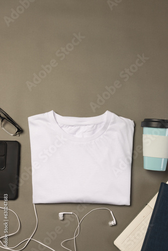 Flat lay of white t shirt, smartphone, earphones and notebooks with copy space on grey background