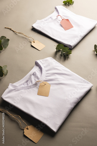 Folded white t shirts with tags and leaves with copy space on brown background
