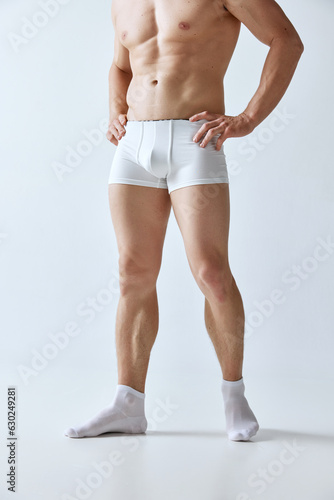 Cropped image of muscular man with relief strong body posing in boxers and socks against grey studio background. Concept of men's beauty, body care, sport, wellness, healthy lifestyle, ad