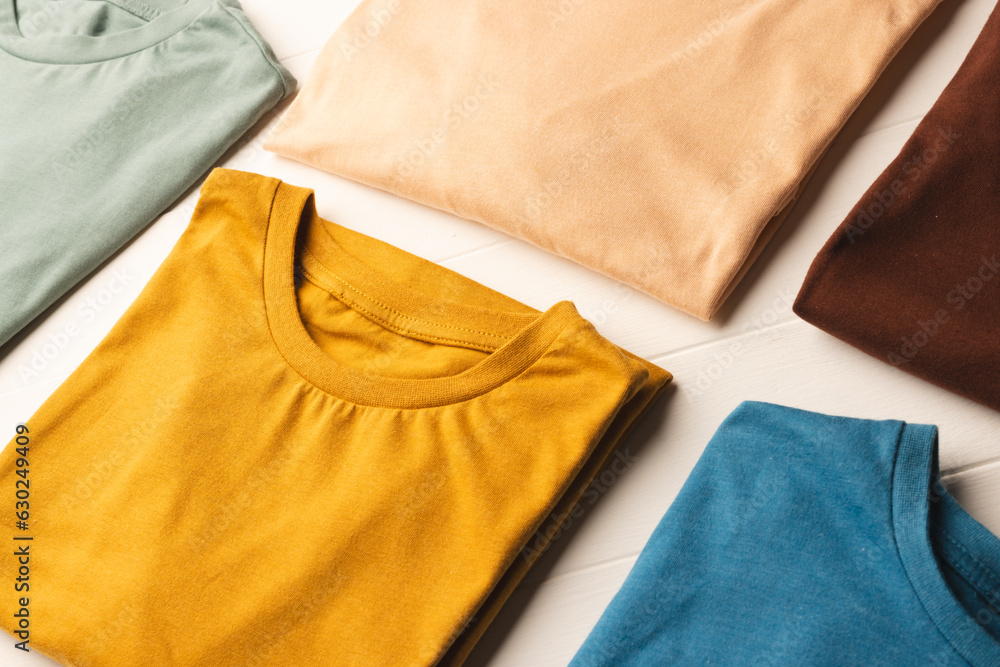 Close up of flat lay of multi coloured t shirts and copy space on white boards background Close up of flat lay of multi coloured t shirts and copy space on white boards background