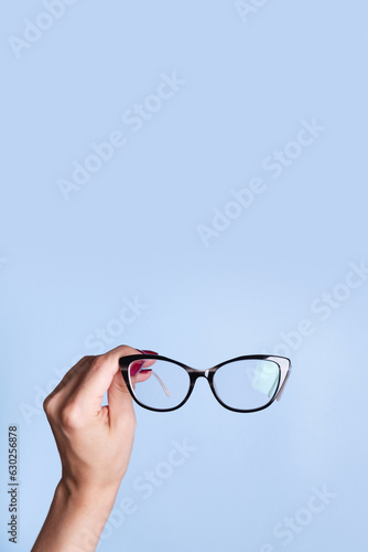 Eyeglasses in female hand on blue background. Optical store, vision test, stylish glasses concept