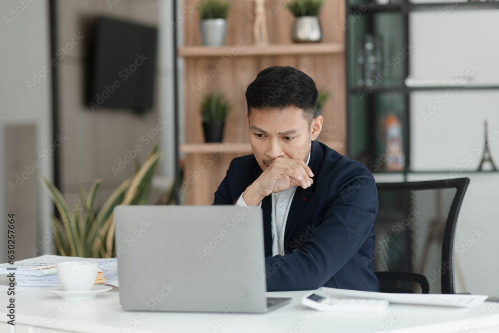 © SOMKID - sad asian businessman sitting at desk in modern office, stressed man, problem, Worried young man businessman,