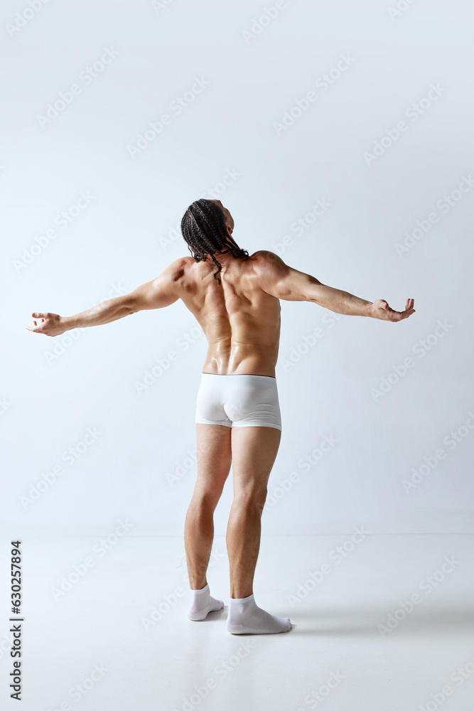 Rear view image of man posing shirtless in underwear against grey studio background. Relief back, muscular, healthy body. Concept of men's beauty, body care, sport, wellness, healthy lifestyle, ad Rear view image of man posing shirtless in underwear against grey studio background. Relief back, muscular, healthy body. Concept of men's beauty, body care, sport, wellness, healthy lifestyle, ad