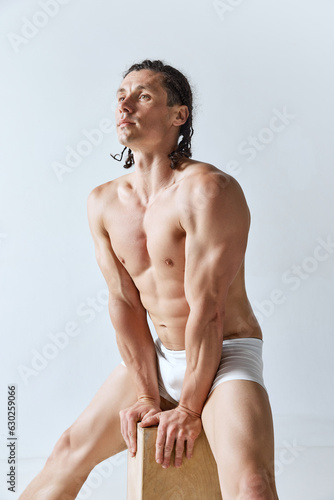 Handsome man with braids posing in underwear against grey studio background. Male model with relief, muscular body. Concept of men's beauty, body care, sport, wellness, healthy lifestyle, ad photo