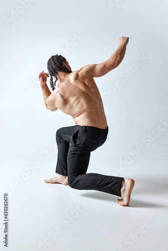 Athletic man posing in motion shirtless, in pants against grey studio background. Healthy, strong, relief body. Concept of men's beauty, body care, fashion, wellness, healthy lifestyle, ad photo