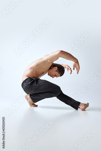 Handsome, athletic man with m,usuclar, reled body posing against grey studio background. Hip hop dancer. Concept of men's beauty, body care, fashion, wellness, healthy lifestyle, ad photo