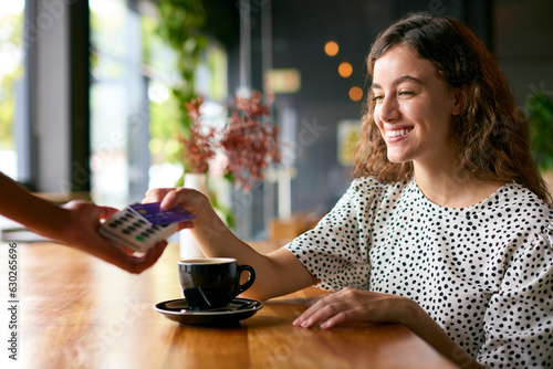 Woman In Coffee Shop Paying Bill With Contactless Card Payment