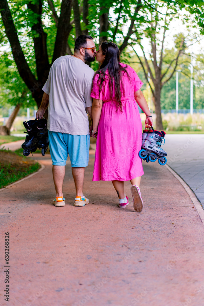 A young couple walks through a park while on a date holding hands and holding rollerblades in the hands of plus size models