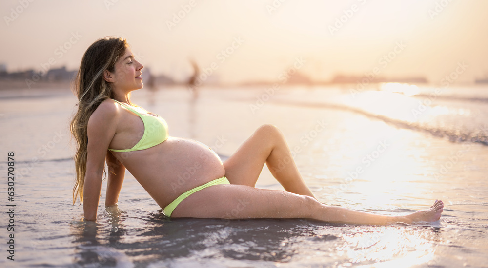 Young pregnant woman relaxing on sandy beach at sunset. Young pregnant woman relaxing on sandy beach at sunset.