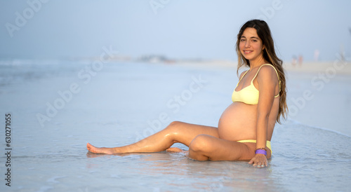 Young 9 months pregnant woman relaxing on sandy beach in summer day.