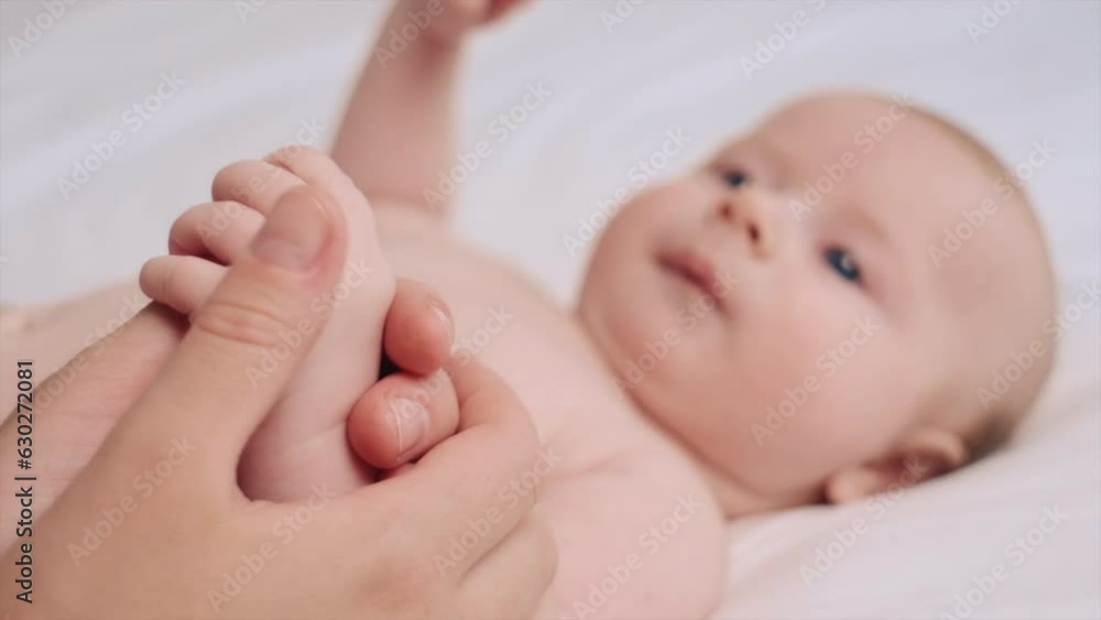 Hand of sweet few month baby resting in mothers palm. Close up of mom holding, touching tiny arm of little cute son. Kid lying on comfortable bed with white sheet. Selective focus. Motherhood concept Hand of sweet few month baby resting in mothers palm. Close up of mom holding, touching tiny arm of little cute son. Kid lying on comfortable bed with white sheet. Selective focus. Motherhood concept