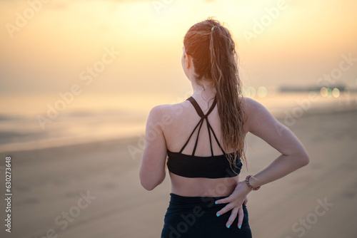 Athletic woman in sportswear standing at the seaside rubbing the muscles of her lower back.