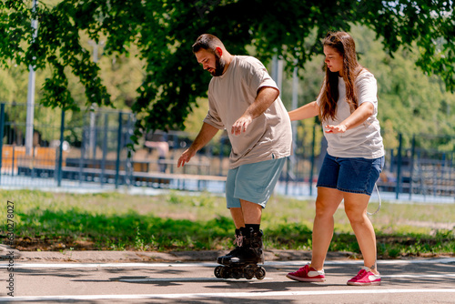 Young couple girl holds hands of the guy who is roller skating and helps him to learn to skate in the park plus size models © Guys Who Shoot