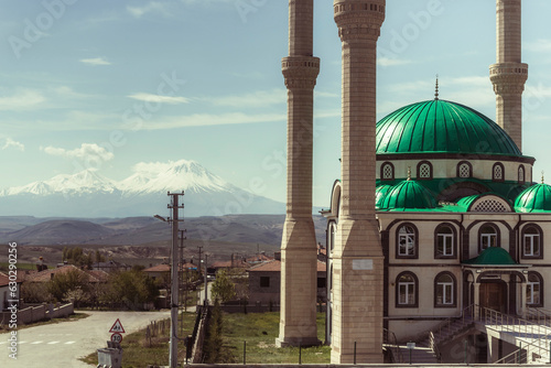 View of Mount Hasandagi, a Mountain Peak and inactive volcano with snow on the top with a green dome mosque in foreground, Aksaray, Turkey. photo