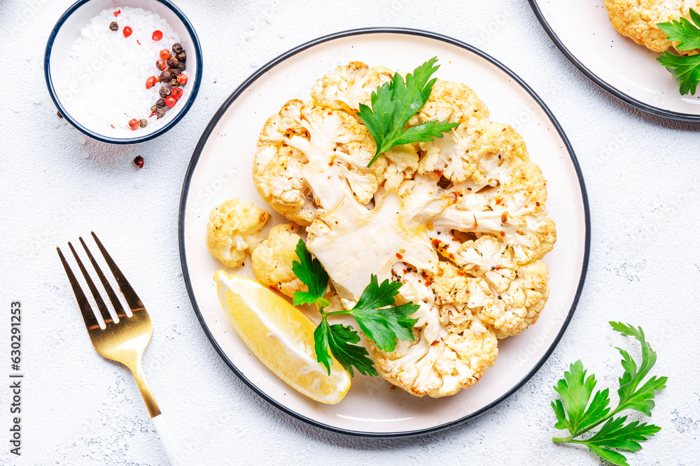 Vegan steak from baked cauliflower with garlic butter, parley and spice on plate, white table background, top view Vegan steak from baked cauliflower with garlic butter, parley and spice on plate, white table background, top view