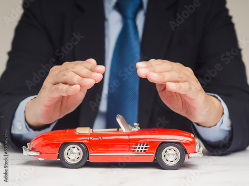 Auto Insurance concept. Businessman hands protection of a red car mockup on a table while sitting at the table.