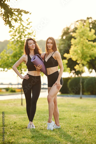 Standing together, with yoga mat. Two women in sport clothes are outdoors on the field