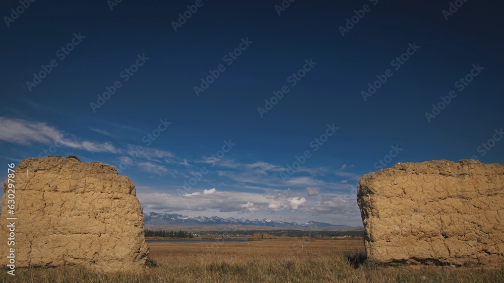 Ancient clay columns the backdrop of snow-capped mountains and clouds. Remains of an ancient dwelling house. Autumn landscape. Tunkinskaya valley, Mongolia Ancient clay columns the backdrop of snow-capped mountains and clouds. Remains of an ancient dwelling house. Autumn landscape. Tunkinskaya valley, Mongolia