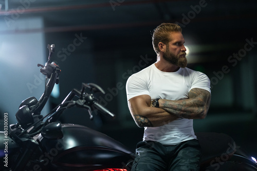 Athletic bearded biker man riding motorbike isolated on indoor parking