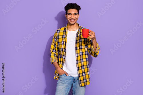 Portrait of funny funky man with stylish earrings wear plaid shirt hold cup of coffee arm in pocket isolated on violet color background © deagreez