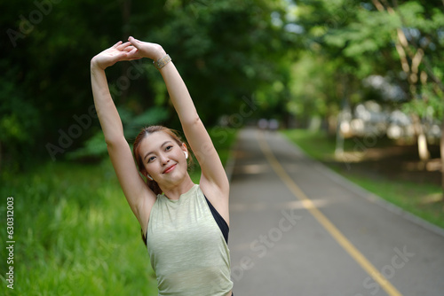 A pretty fitness female doing stretching exercises and smiling to enjoy morning jogging in the park.