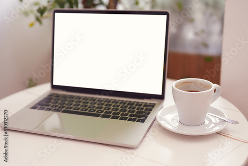 Blur laptop computer with blank white screen with coffee cup on white table background. Working business concept.
