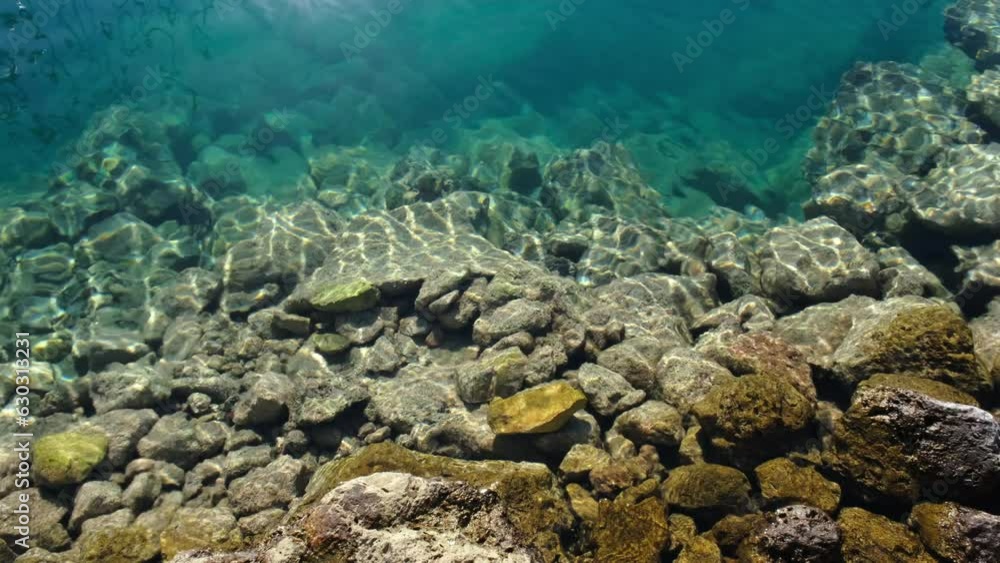 Many stones in clean transparent blue sea water. Sun rays on the ocean bottom Many stones in clean transparent blue sea water. Sun rays on the ocean bottom