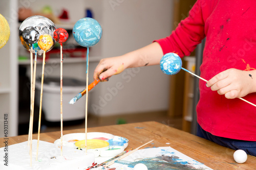 Boy painting styrofoam balls when making model of Solar System for school. Science project at home. Concept of teaching children. Developing creativity from an early age. Drawing with brushes and pain