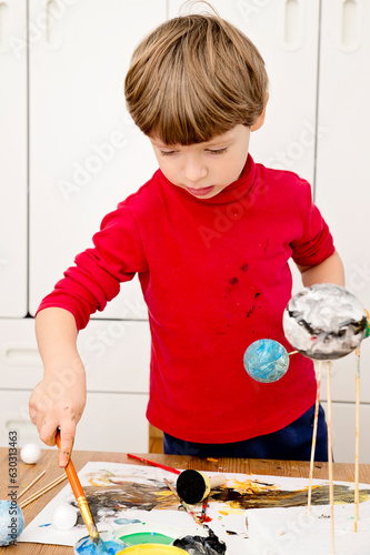 Boy painting styrofoam balls when making model of Solar System for school. Science project at home. Concept of teaching children. Developing creativity from an early age. Drawing with brushes and pain