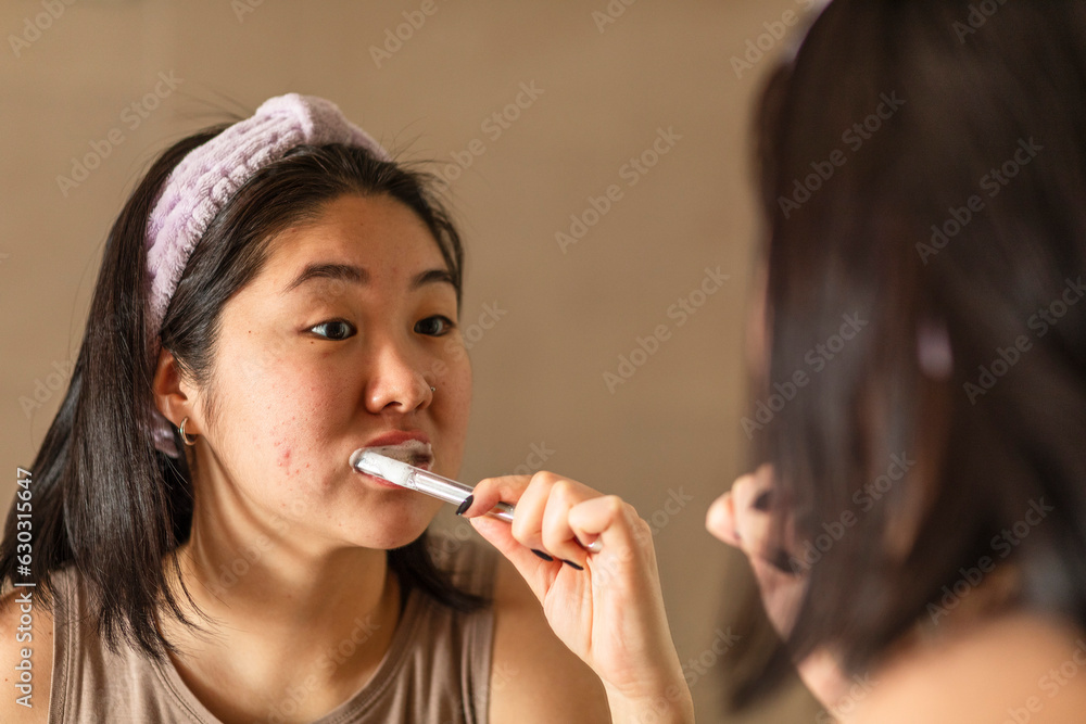 asian girl in hairband brushing teeth in front of the mirror in the bathroom, morning routine concept asian girl in hairband brushing teeth in front of the mirror in the bathroom, morning routine concept