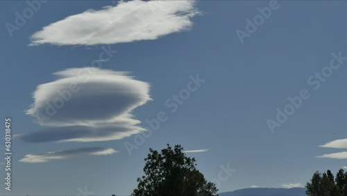 Blue sky with moving Lenticular clouds, Lenticularis lentil shaped during Foehn wind. Weather phenomenon over horizon of Silesian Beskid mountains in Poland on windy day - timelapse. photo