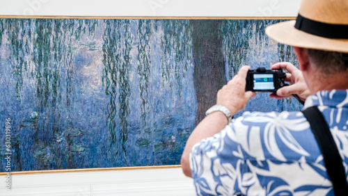 Tourist photographing a large impressionist painting at the Museum de l'Orangerie in Paris