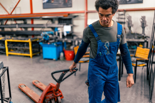 A mixed race worker in overalls pulls a small forklift for transport