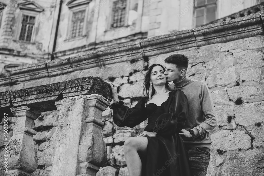 Newlyweds kissing. Female embrace male wall in street. Luxury couple near old Pidhirtsi Castle. Woman in dress hugs man on stairs near ancient palace at sunset. Bride hug groom. Black and groom photo