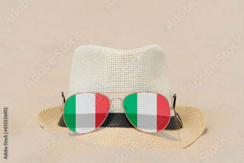 Fototapeta Naklejka Na Ścianę i Meble -  Sunglasses with glasses in the form of the flag of Italy and a hat lie on the sand. The concept of summer holidays, travel and tourism in Italy