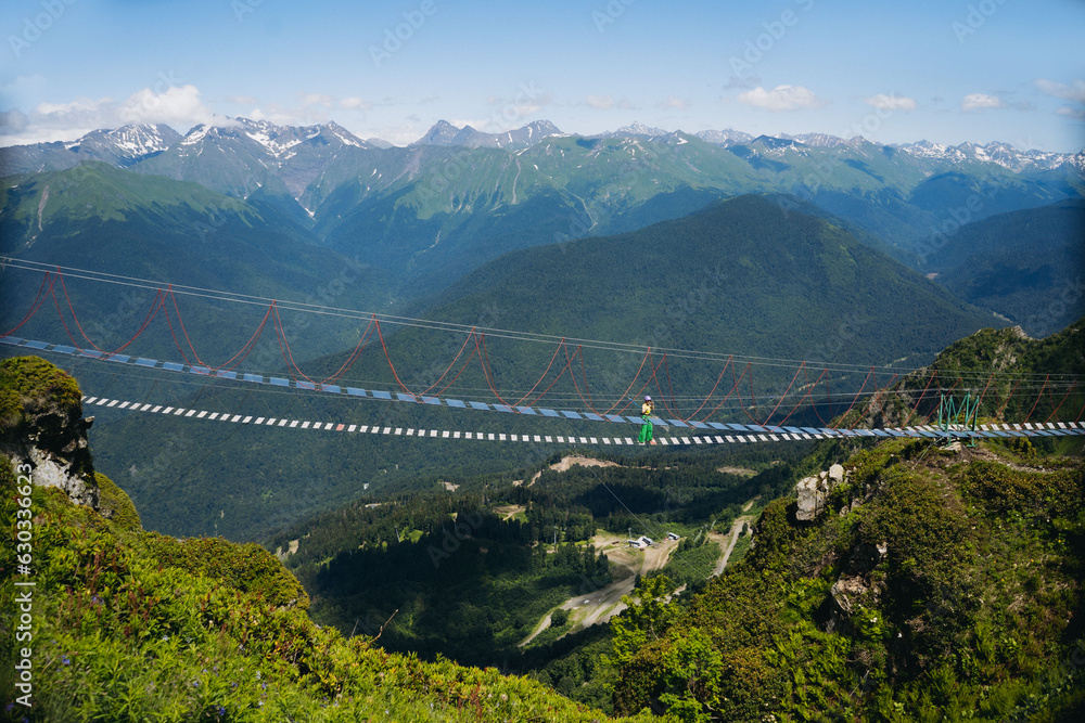 woman tourist walking on rope suspension bridge in caucasus mountains, Russia, Rosa Khutor resort