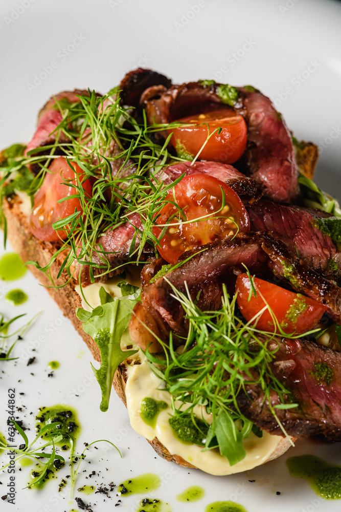 Bruschetta with meat, tomatoes, herbs, cheese, pesto sauce on a white plate. Bruschetta with meat, tomatoes, herbs, cheese, pesto sauce on a white plate.