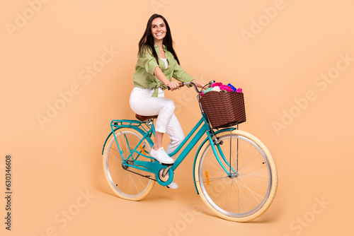 Fototapeta Naklejka Na Ścianę i Meble -  Full size photo of optimistic girl dressed green blouse white trousers riding bicycle on weekends isolated on beige color background