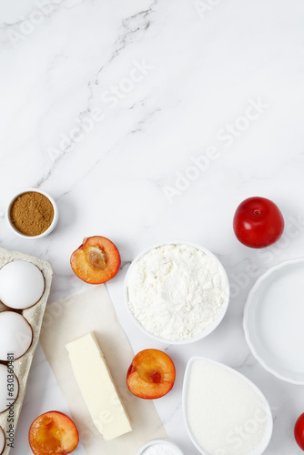 Ingredients for making classic cake pie with plums on white background. Concept homemade food, seasonal pastries. Top view, copy space