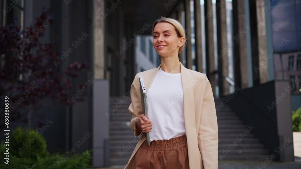 Female confident corporate office woman employee in formal suit holding a laptop in hands walking along the street. An attractive and beautiful businesswoman outside the commercial complex. Female confident corporate office woman employee in formal suit holding a laptop in hands walking along the street. An attractive and beautiful businesswoman outside the commercial complex.