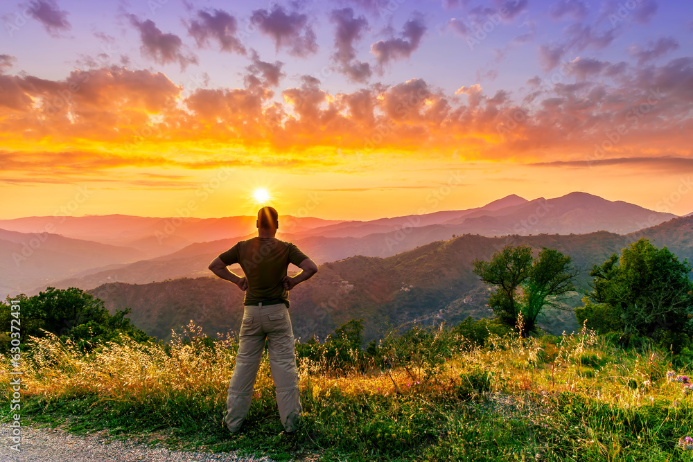 Fototapeta premium rejoicing man with beautiful scenic mountain sunset landscape on background. happy man watching amazing evening sunset