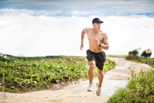Athletic healthy man running in mountain with clouds landscape background. Fitness Asian trail runner male sprinting outdoors. Full length shot. Healthy lifestyle