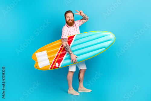 Full length profile portrait of eccentric funky guy hold inflatable surf board mattress demonstrate v-sign isolated on blue color background