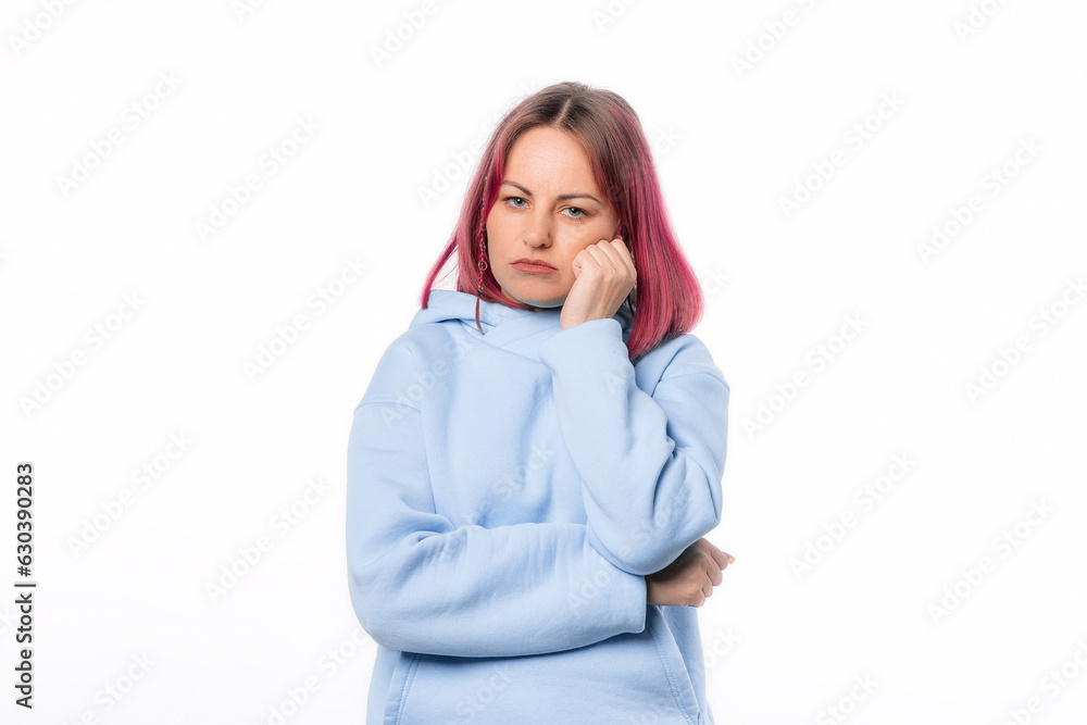 Bored woman thinking about relationships, leaning face on palm, standing with indifferent annoyed expression. Lovely female model with pink hair in a blue hoodie standing over white background Bored woman thinking about relationships, leaning face on palm, standing with indifferent annoyed expression. Lovely female model with pink hair in a blue hoodie standing over white background