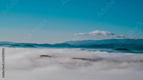 Landscape featuring mountains and fluffy white clouds against a backdrop of a bright blue sky.