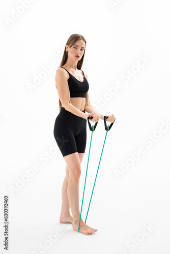 Beautiful girl in sportswear is training with an expander on a white background