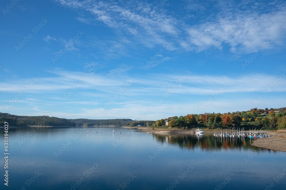 Shore of lake surrounded by fall colored trees and a blue sky in the background